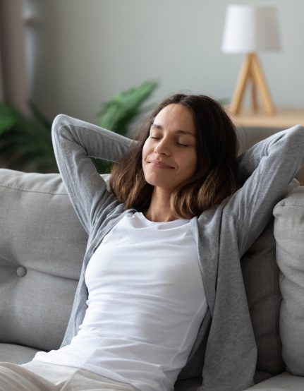 Tranquil smiling biracial millennial woman leaning on sofa, enjoying stress free weekend time at home. Mindful happy mixed race young girl relaxing in living room, meditating, visualizing future.